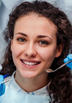 woman in dental chair smiling while getting cosmetic dental bonding