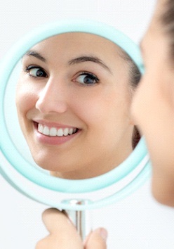 A young female looking at her new appearance in the mirror after undergoing a smile makeover