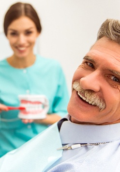 An older man smiling while a dental hygienist explains how to maintain his new and improved smile