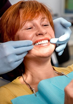 An older woman with red hair looking at her smile in the mirror as a dentist explains what work needs to be done