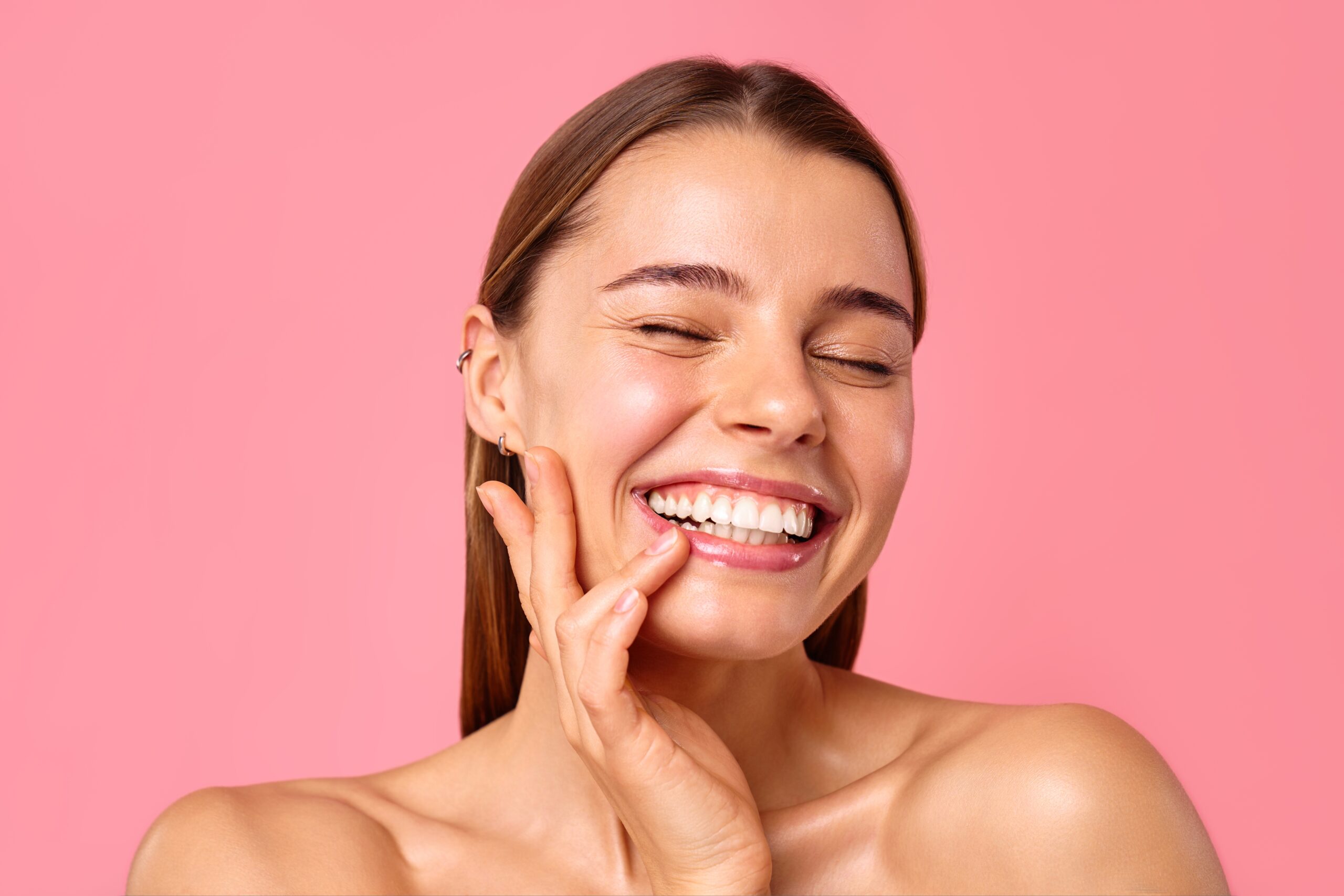 A woman smiles wide while holding her cheek to show off her big beautiful smile