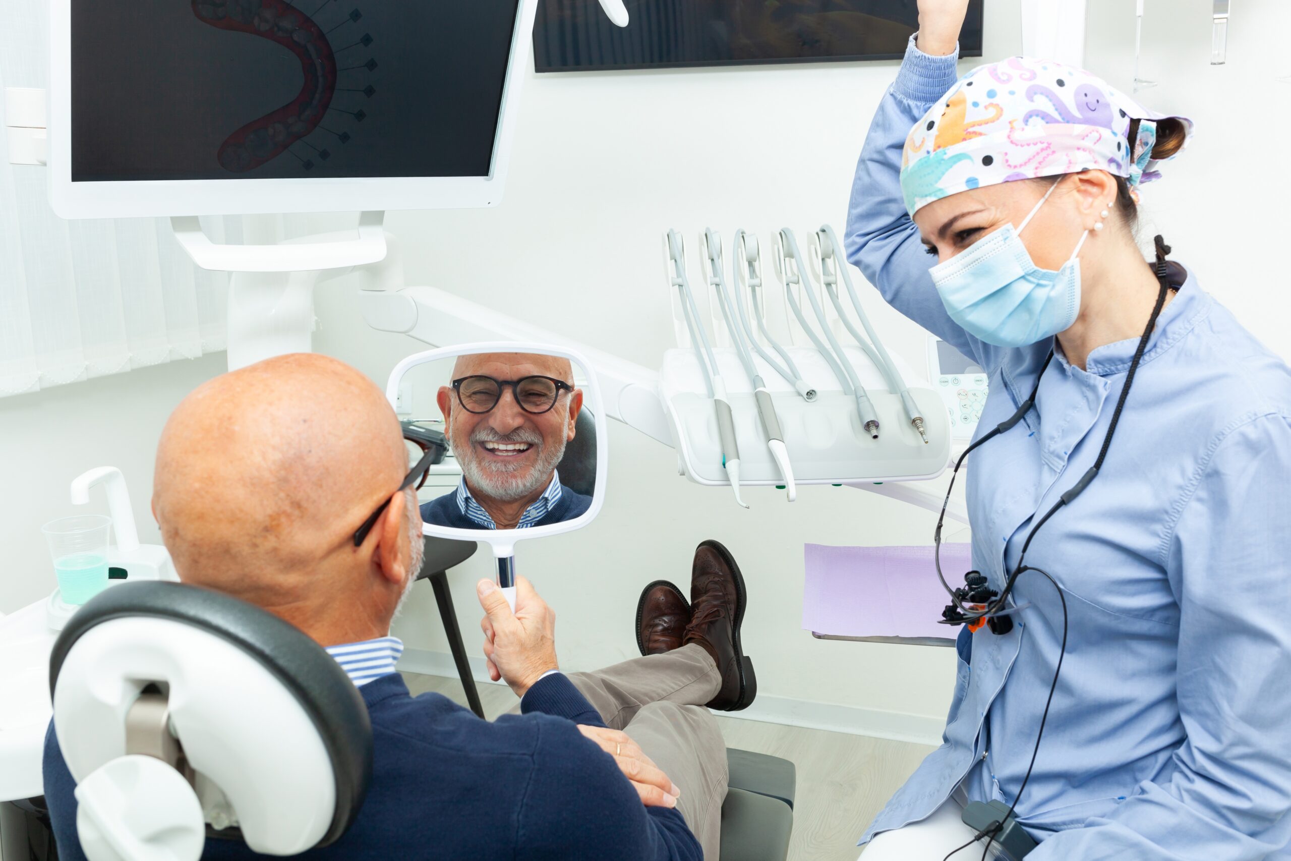 man smiling in a mirror, happy with his implant-supported dentures