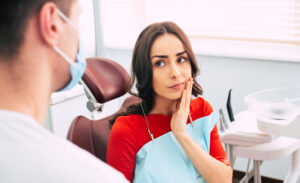 young woman sitting in a dental chair with her hand on her jaw