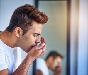 man blowing into his hand, checking for bad breath