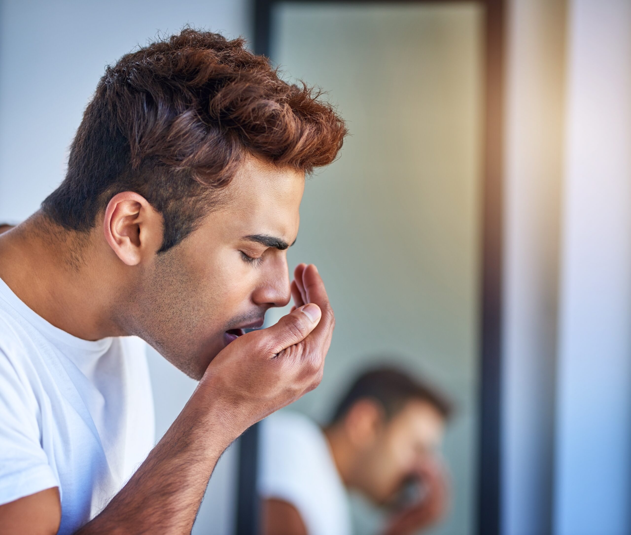 man blowing into his hand, checking for bad breath