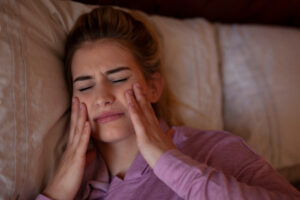 young woman lying down struggling with jaw and head pain