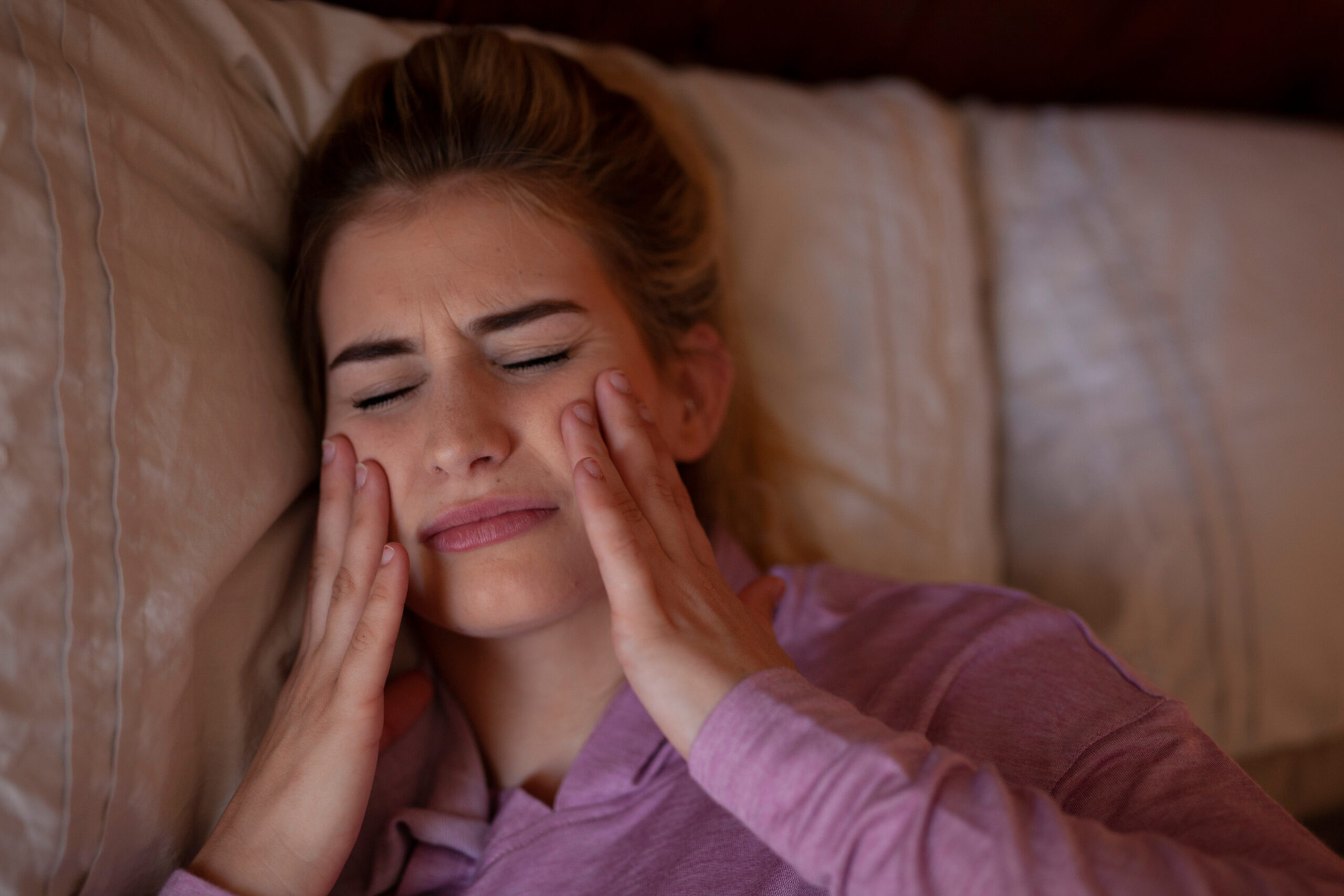 young woman lying down struggling with jaw and head pain