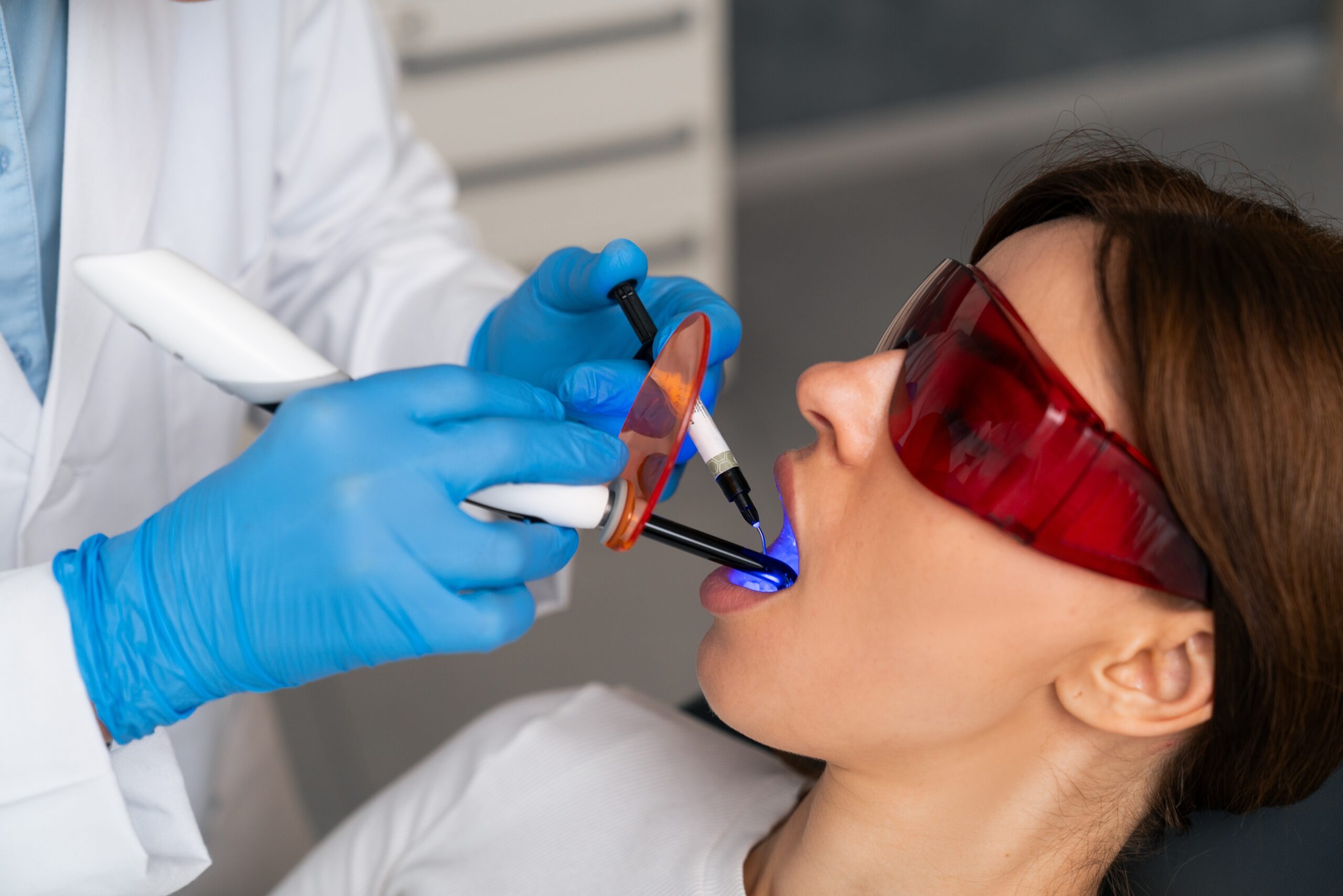 dentist in blue gloves using a dental laser on a female patient